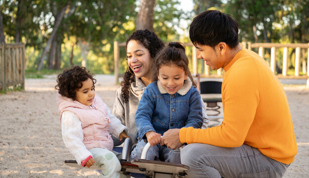 Smiling latin parents enjoying playtime with daughters on seesaw in park