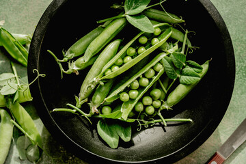 Fresh green peas in pods and beans in a black bowl