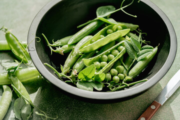 Fresh green peas in pods and beans in a black bowl