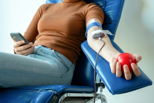 Relaxing Woman Donating Blood Holding Stress Ball Using Cellphone on Blue Chair - Powered by Adobe