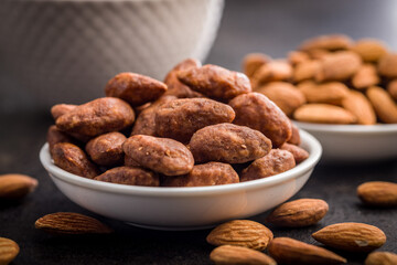 Almond nuts coated in sugar and honey in bowl on black table.