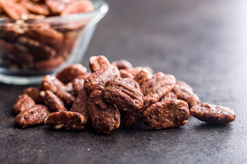 Pecan nuts coated in sugar and honey on black table.