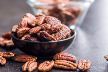 Pecan nuts coated in sugar and honey in bowl on black table.