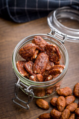 Pecan nuts coated in sugar and honey in jar on wooden table.