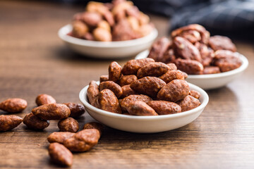 Almond nuts coated in sugar and honey in bowl on wooden table.