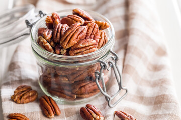 Peeled pecan nuts in jar on white table.