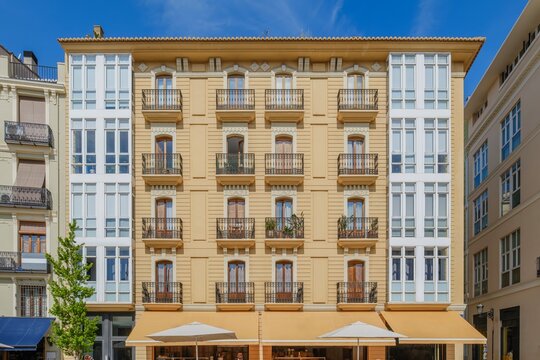 An elegant residential building facade in Valencia, Spain, featuring symmetrical balconies with wrought iron railings and classic European architecture - Powered by Adobe