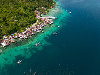 Fishing boat over the blue sea and stilt houses on turquoise ocean water. Mindanao, Philippines.
