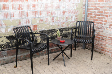 There are two chairs along with a table positioned in front of a brick wall