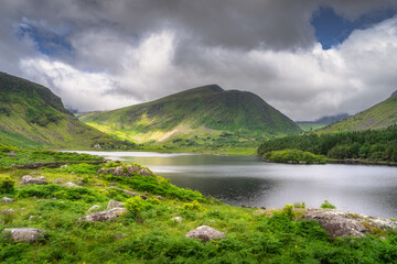 A stunning mountain landscape features a beautifully tranquil lake, lush vibrant greenery of Black Valley and impressive clouds, showcasing the breathtaking beauty of nature all around, Kerry, Ireland