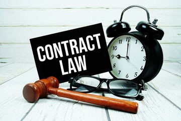 Contract Law text on paper card with alarm clock and wooden judge gavel on wooden background