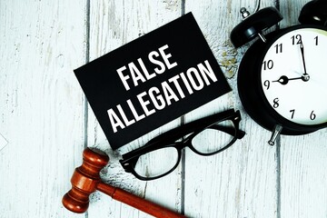 False Allegation text on paper card with alarm clock and wooden judge gavel top view on wooden...