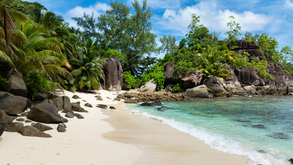 A white sandy beach with turquoise water, surrounded by lush green vegetation. Butzel Beach. Seychelles, Mahe.