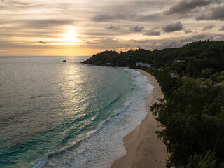 The sun sets over a serene coastline with gentle waves, reflecting golden hues. Anse Intendance. Seychelles, Mahe.