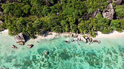 Turquoise waters of the shoreline with rocky formations surrounded by lush greenery. La Digue, Seychelles.