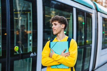 Young college student waiting for the tram with his binder and backpack