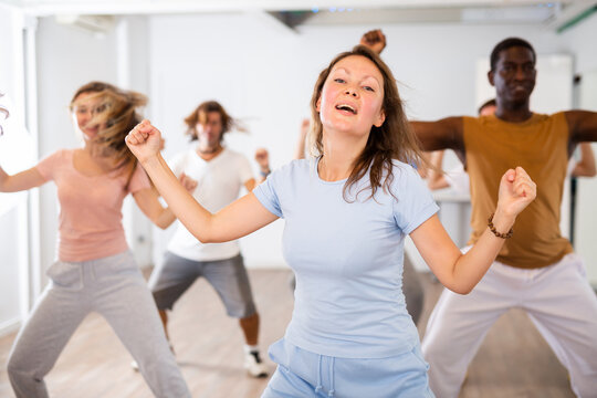 Group of excited young adult diverse dancers performing dynamic movements during training together in fitness studio