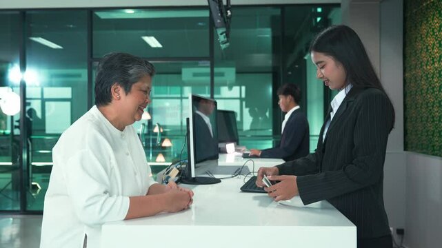 Senior Passenger at Airport Check-In, Asian Woman Verifying Passport with Friendly Airline Staff for International Travel at Departure Counter