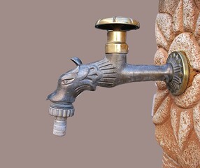 A garden tap shaped like an animal head, mounted on a reddish-white terracotta wellhead, with a partial handle, close-up shot, against a gray, monochrome background.