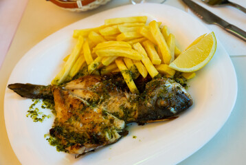 Baked in oven dorado fish with lemon and french fries served on plate