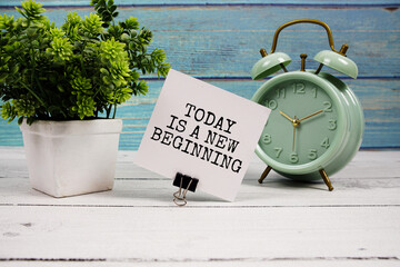 Today is a new beginning  text written on paper card with alarm clock on wooden background