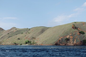 Discover the breathtaking rolling hills of Gili Lawa, Indonesia, meeting the deep blue sea. A stunning landscape perfect for your adventurous escape.  © Ading