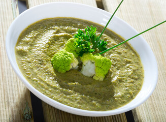 Healthy broccoli cream soup served in white bowl with greens