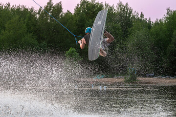 Wakeboarder making tricks. Low angle shot of man wakeboarding on a lake. Man water skiing at sunset.