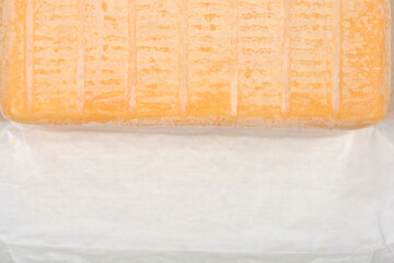 Close-up shot captures the textured rind of a Limburger cheese block resting on a simple white...
