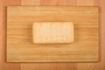 A top-down shot of a rectangular block of Limburger cheese placed on a wooden cutting board