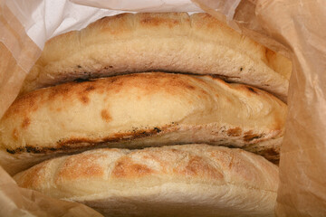 Three freshly baked flatbreads, partially wrapped in brown paper