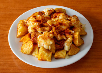 A plate of patatas bravas with aioli and spicy paprika on a wooden table, a typical Spanish tapa
