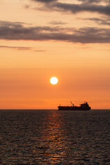 Obraz premium Vertical shot of a seascape with a cargo ship in the Baltic Sea at sunset. An evening off the coast of Estonia, with the sun above the horizon.