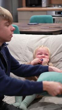 Crying baby is comforted byn older sibling who first tries to give the baby a mustache and then embraces the child tenderly