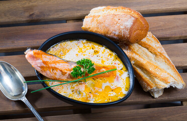 Traditional Norwegian creamy soup with salmon served in black bowl with freshly baked baguette ..