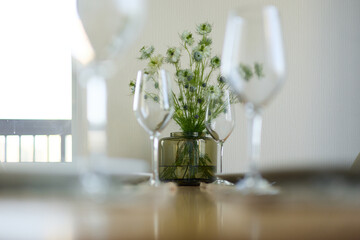 a bouquet of daisies in a glass vase stands on a table on a white background, a wine glass, table setting, plates, defocus, macrophotography, bokeh