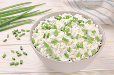 Farm cheese in a bowl on a light wooden background. Cottage cheese with young green chives.