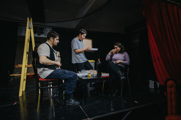 A group of young actors practicing a scene on stage. The setting includes theatrical props and...
