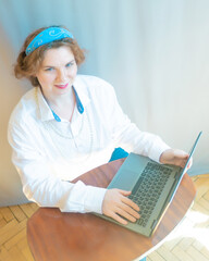 A beautiful young woman is working or playing or shopping on a laptop in a stylish white shirt and a hair band in the shape of the Russian national kokoshnik headdress