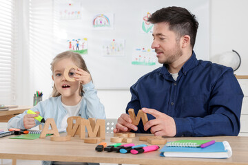 Little girl learning letters with teacher at desk indoors