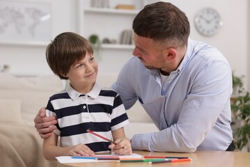Father teaching his son to draw at table indoors