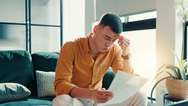 Stress, man and reading document at house financial crisis, payment notice and debt pressure. Frustrated, male person and paperwork for bank repossession, loan rejection and eviction letter in lounge