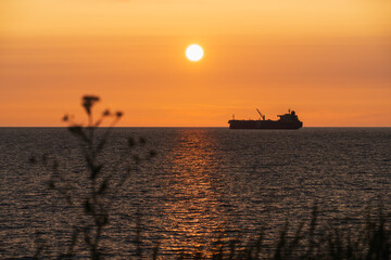 Orange sunset over the Baltic Sea with the silhouette of an oil tanker on the horizon. Evening seascape from the coast of Estonia.