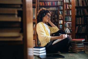 Listening to music and writing. Beautiful woman is in the library