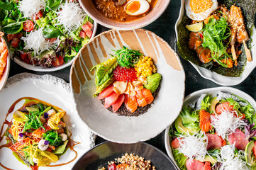 colorful assortment of Japanese-inspired dishes, including poke bowls, ramen, and fresh salads, featuring salmon, tuna, avocado, vegetables, and garnishes, arranged in visually appealing presentation