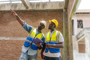 An African male engineer is overseeing the construction of a building with construction workers who...