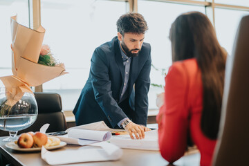 Two colleagues engaged in a workplace discussion examining documents and planning strategies in a...