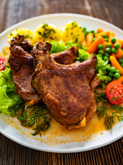 Baked veal chops, boiled potatoes, green peas and carrots on wooden table