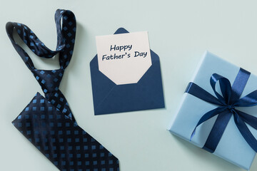 Greeting card with blue gift, necktie, sheet on blue background. Men's accessories set. Top view....
