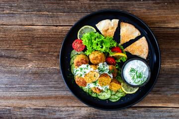Fried meatballs with tzatziki sauce and pita bread on wooden table. Greek style food